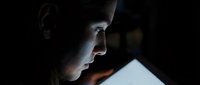 Young Caucasian woman illuminated by screen glow in dark room, focused expression conveying concentration, technology use, or late-night work.
