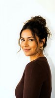 Young Hispanic woman with messy bun hairstyle wearing brown ribbed sweater smiling at camera against white background for lifestyle photography.