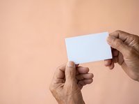 Close-up of male hands with medium skin tone holding blank white card against neutral beige background, suitable for business card mockups and corporate branding presentations.