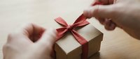 Hands tying red ribbon bow on kraft gift box for holiday present wrapping and celebration occasions.