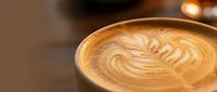 Latte art with leaf design in ceramic cup on wooden surface, suitable for coffee shop marketing and beverage advertising.