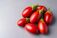 Fresh red plum tomatoes with green stems arranged on light gray background, macro food photography showing vibrant color and texture for cooking and recipes.