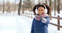 Happy African American girl in winter coat and headphones enjoying snowy park day with warm smile and playful gesture for seasonal lifestyle content.