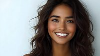 Young Hispanic woman with long wavy dark hair and bright white smile against light background, radiating confidence and joy in casual portrait style.