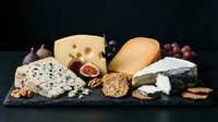 Gourmet cheese platter with variety of artisanal cheeses, nuts, grapes and crackers on dark slate board for culinary presentations and food styling.
