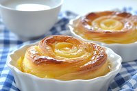 Fresh baked apple rose tart with caramelized layers of thinly sliced fruit arranged in spiral pattern, served in white ramekin on blue checkered cloth.
