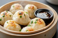 Pan-fried dumplings garnished with chopped green onions served in traditional bamboo steamer basket with dark soy dipping sauce, close up view of Asian cuisine.