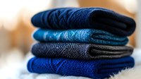 Neatly folded stack of blue and navy knitted winter socks with textured patterns, arranged in gradient shades against soft blurred background.