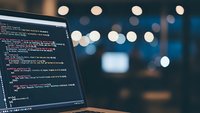 Software developer programming code on laptop screen in modern office environment with bokeh lights background for technology projects.