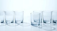 Empty clear glass tumblers arranged in rows on white surface with soft lighting and reflections for kitchen and dining concepts.