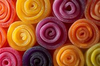 Colorful spiral jelly candy rolls covered in sugar crystals arranged in rows showing vibrant orange, yellow, pink and purple sweet treats in macro photography.