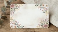 Blank floral greeting card with watercolor pink flowers and green leaves on corners, displayed on wooden surface with fabric and eucalyptus for wedding, invitation, or stationery design.