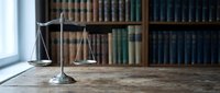 Scales of justice on wooden desk in law library with vintage books background for legal concepts and attorney office decor.