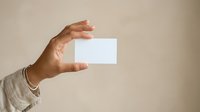 Hand holding blank white business card against neutral beige background, ready for branding and contact information design.