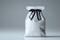 White fabric gift bag with black ribbon drawstring closure on gray background, elegant minimalist packaging design for presents and retail products.