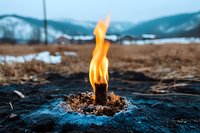 Natural gas flame erupting from ground in snowy mountain landscape, burning orange fire against dark soil and dry grass, dramatic environmental scene.