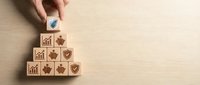 Hand placing wooden cube with checkmark on pyramid of business icon blocks representing quality control and achievement on wood background.