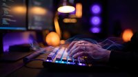 Hands typing on illuminated keyboard with colorful LED backlighting in dark gaming setup. Night work, programming, esports and technology concept for digital lifestyle.