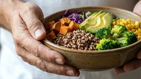 Mature man holding bowl with quinoa, roasted sweet potato, purple cabbage, corn, broccoli and avocado. Healthy meal prep and balanced nutrition concept.