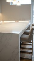 Modern kitchen island with white quartz countertop and marble-look base in contemporary home interior with pendant lighting and bar stools.