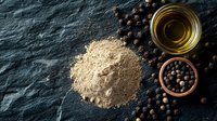 Ground black pepper powder with whole peppercorns and olive oil on dark stone background. Culinary spices and seasonings composition.