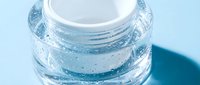 Clear glass cosmetic jar with white lid containing blue skincare cream or gel product on clean background for beauty and wellness applications.