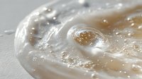 Translucent gel-like substance with golden particles suspended in clear viscous fluid, showcasing texture and bubbles in macro photography.