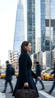 Professional businesswoman walking through busy urban street with skyscrapers and yellow taxis in motion blur background for corporate lifestyle concepts.