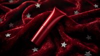 Red lipstick on dark burgundy velvet fabric with scattered silver stars creates luxurious cosmetic composition for beauty and fashion concepts.