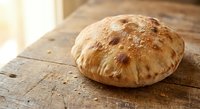 Freshly baked artisan bread loaf with golden crust on rustic wooden table. Homemade bakery product for cooking and food photography projects.