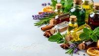 Natural essential oils in glass bottles with fresh herbs, lavender, mint, cinnamon sticks and dried citrus slices for aromatherapy and wellness treatments.