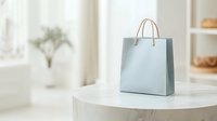 Light blue shopping bag with brown handles on white round table in bright minimalist interior setting, soft natural lighting creates elegant retail atmosphere.