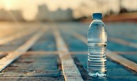 Water bottle on blue tiled surface at sunset with urban skyline in background, symbolizing hydration and fitness lifestyle.