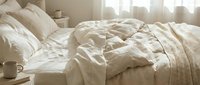 Unmade bed with cream linen sheets and pillows in bright morning sunlight, ideal for home decor, lifestyle, and bedroom interior design projects.