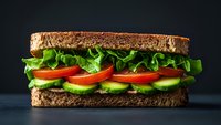 Fresh vegetarian sandwich with lettuce, tomato and avocado on whole grain bread against dark background for healthy eating and food photography.