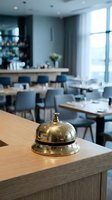 Shiny brass service bell on a wooden hotel reception counter with a blurred modern restaurant interior in the background.