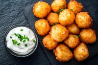 Deep fried potato croquettes served on black slate with sour cream dip garnished with fresh chopped chives. Traditional appetizer for restaurant menu.