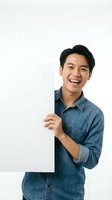Young Asian man wearing denim shirt holding blank white sign, smiling at camera against white background. Isolated cutout ready for design, advertising, marketing materials.