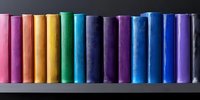 Row of colorful book spines arranged in rainbow spectrum order on dark shelf, creating vibrant educational and literary display for library or bookstore concepts.