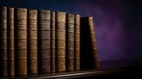 Row of antique leather-bound books on wooden shelf against dark purple background for vintage library and education concepts.