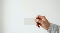 Male hand holding blank white business card against neutral background for corporate branding and marketing mockup purposes.
