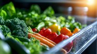 Fresh organic vegetables in refrigerator drawer with water drops, including broccoli, carrots, tomatoes and leafy greens for healthy eating and storage.