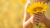 Child holding bright yellow sunflower outdoors in natural sunlight. Warm, cheerful summer scene perfect for family, nature, and happiness-themed designs.