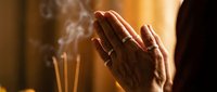 Hands in prayer position with burning incense sticks creating aromatic smoke in warm golden light for meditation and spiritual wellness practices.