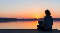 Woman meditating on wooden dock at sunset over calm lake. Peaceful mindfulness practice during golden hour for wellness and relaxation concepts.