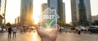 Young adult hand holding glowing holographic house icon with 2027 and checkmark over urban cityscape at sunset, representing future real estate investment and property growth.