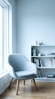 Modern minimalist reading corner with blue upholstered chair and white bookshelf by window in contemporary home interior design for relaxation space.