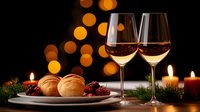 Festive holiday table setting with wine glasses, fresh bread rolls and cranberries against glowing bokeh lights and burning candles creating warm ambiance.