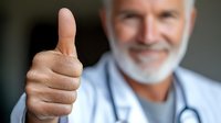 Senior male doctor with gray beard wearing white coat and stethoscope showing thumbs up gesture while smiling at camera, expressing positivity and confidence.