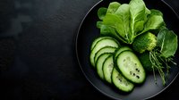 Fresh green salad with sliced cucumber and leafy greens on dark plate against textured black background for healthy eating and diet concepts.